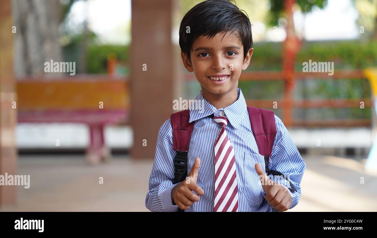 Smiling Indian Rural school boy with backpack looking at camera. Cheerful kid wearing school uniform with a big smile. Elementary and primary school e Stock Photo