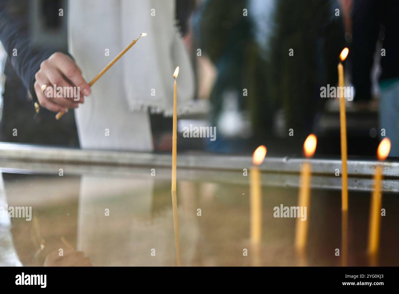 Iryna, a Ukrainian refugee, lights a candle in a chapel of the Orthodox monastery Putna. After Russia invaded Ukraine, in 2022, two Ukrainian families found refuge in Putna Orthodox monastery in Romania: Iryna B., a former English teacher, her mother-in-law Natalia, her best friend also named Iryna, and their five children. 24 kilometers from the Ukrainian border, they fill their days with online education, calls to relatives, walks and prayers. Stock Photo