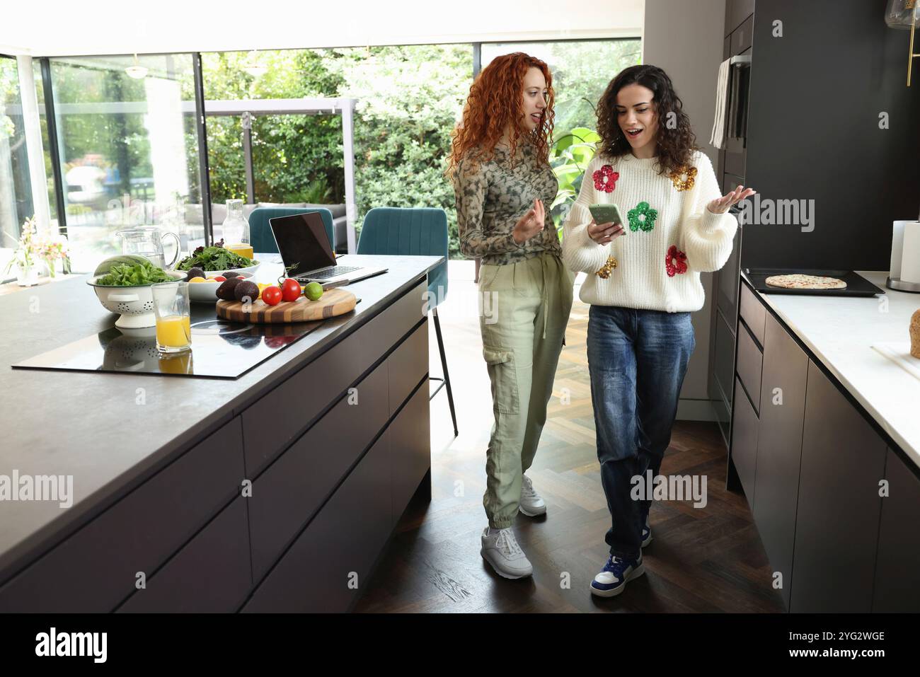 Two women checking on phone in kitchen Stock Photo