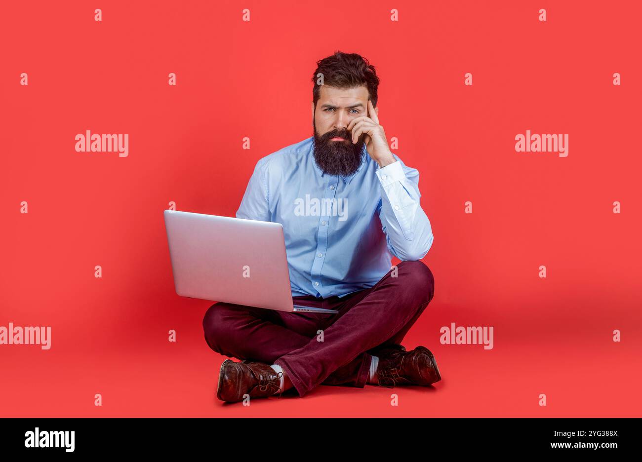 Man working on laptop. Beard man sitting on the floor with and using laptop computer on red background. Holding laptop computer. Businessman using his Stock Photo
