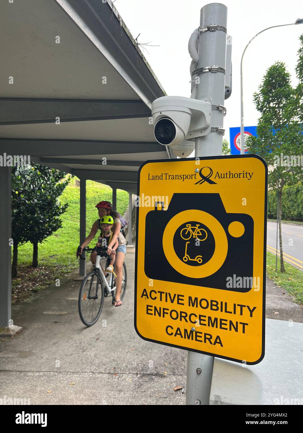 Mother and son wear helmet while cycling through the shelter path while an active mobility enforcement camera is monitoring the walkway, Singapore. - Smartphone Captured Stock Image
