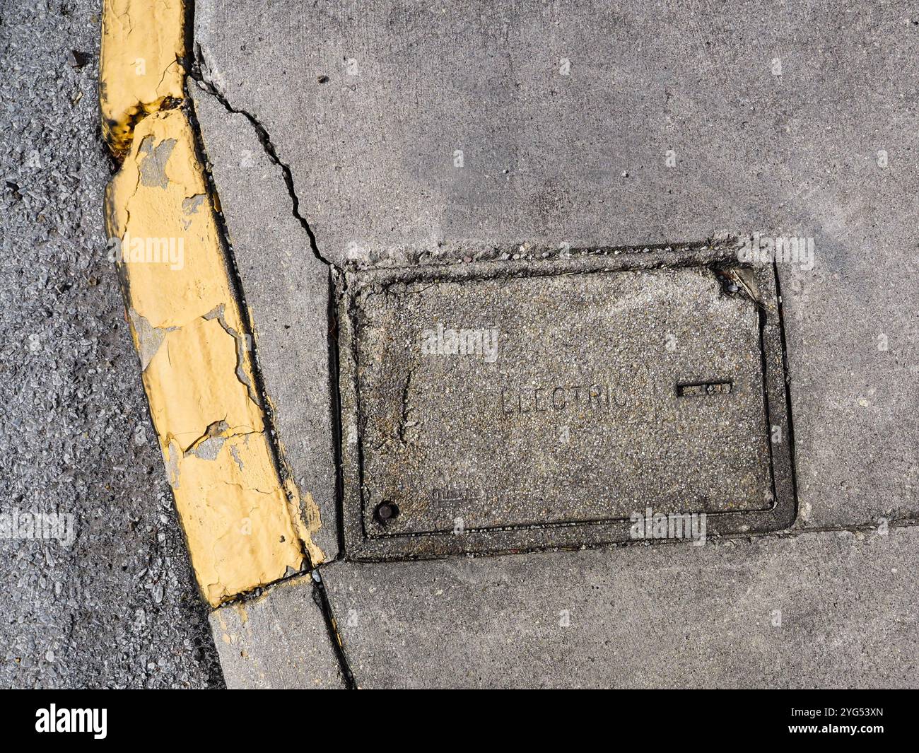 Cracked pavement with a yellow curb and underground electric access ...
