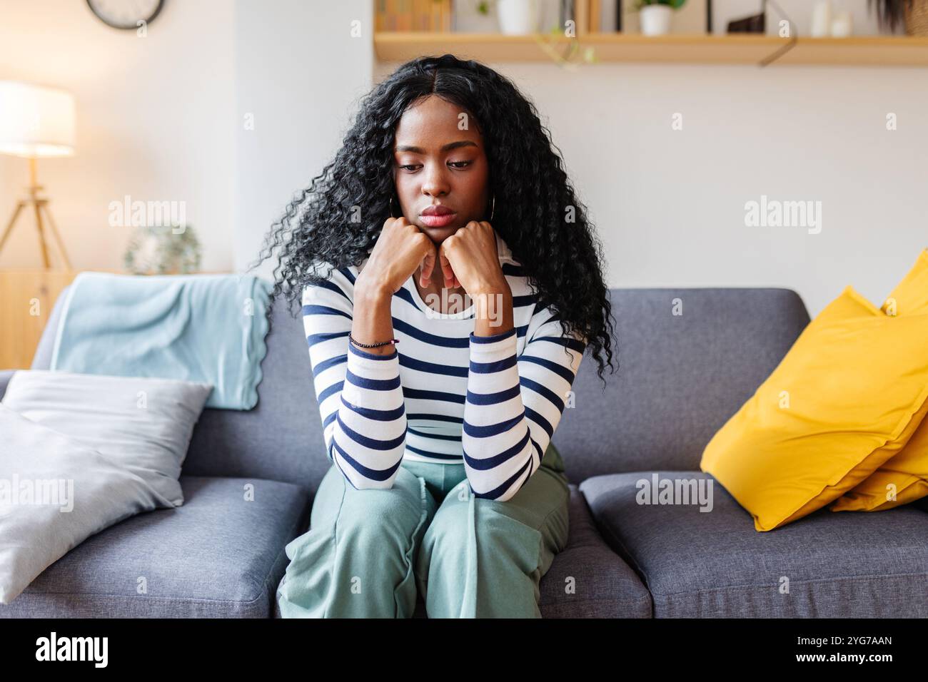 Sad african american woman sitting on sofa resting chin on hands Stock ...