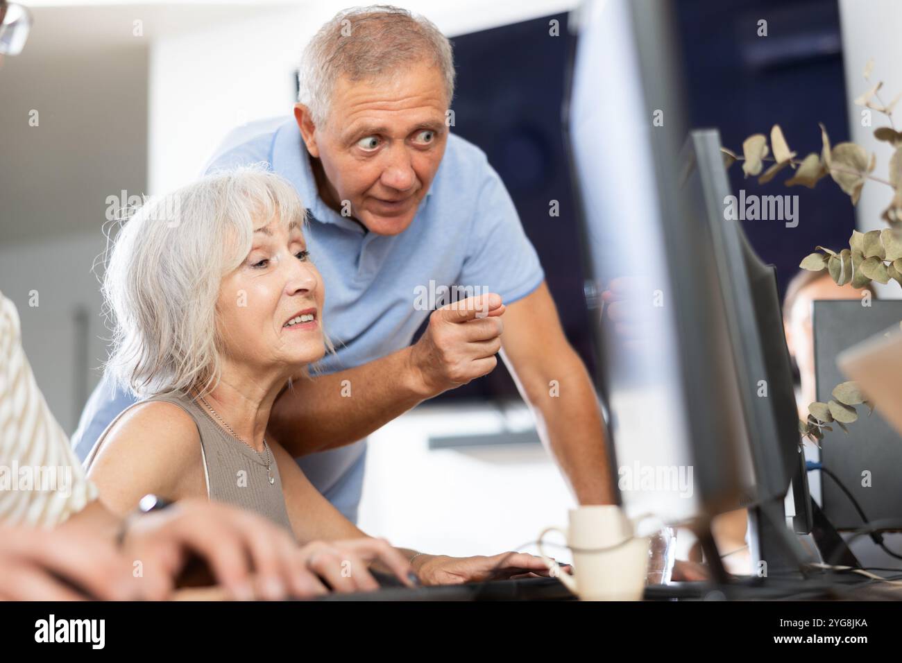 Older mentor explaining something to elderly woman during computer class Stock Photo