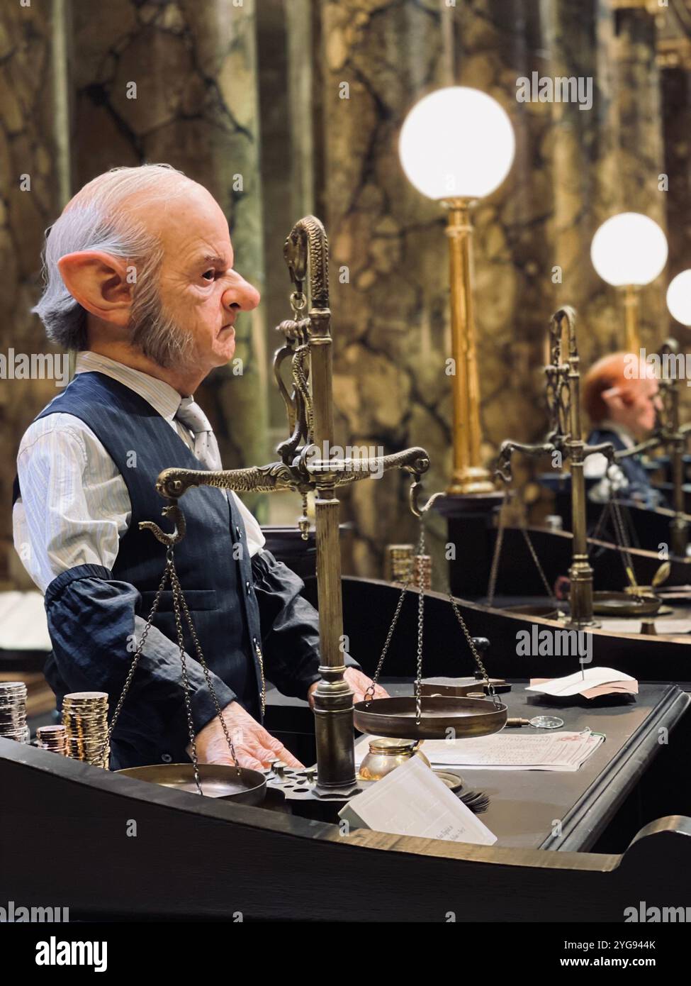 A detailed image of a goblin-like character working as a banker, with a focused expression, standing at a counter adorned with scales and stacks of co - Smartphone Captured Stock Image