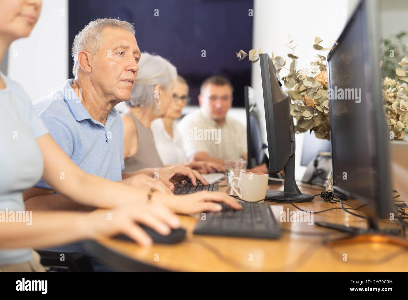 Focused older gentleman using computer at internet cafe Stock Photo