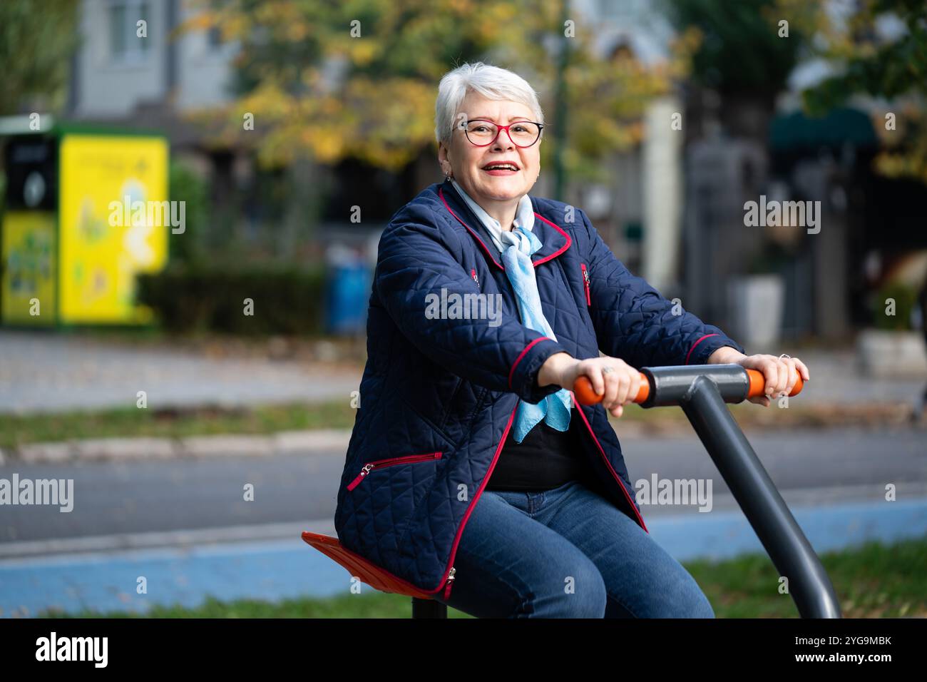 A senior woman in a blue jacket and scarf uses an exercise simulator in ...