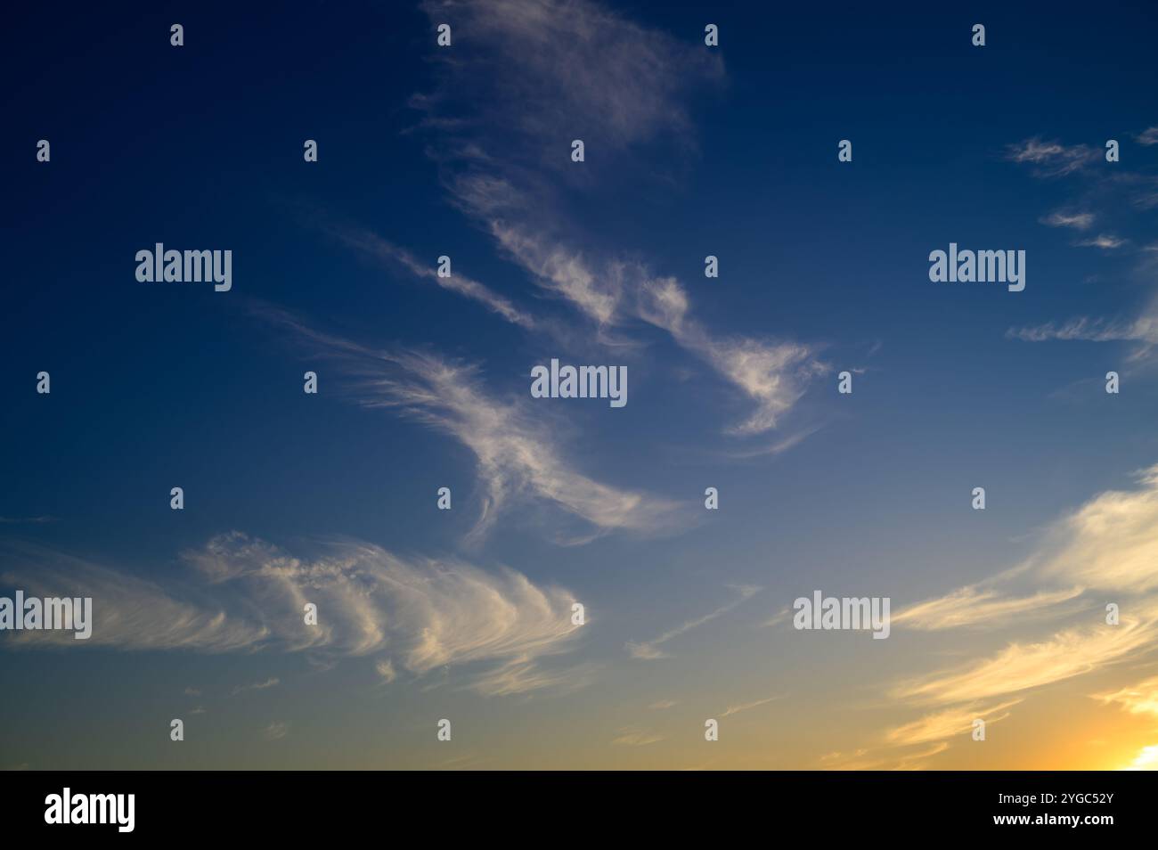 Delicate cloud formations create a mesmerizing pattern against a vibrant evening sky as the sun sets. Stock Photo