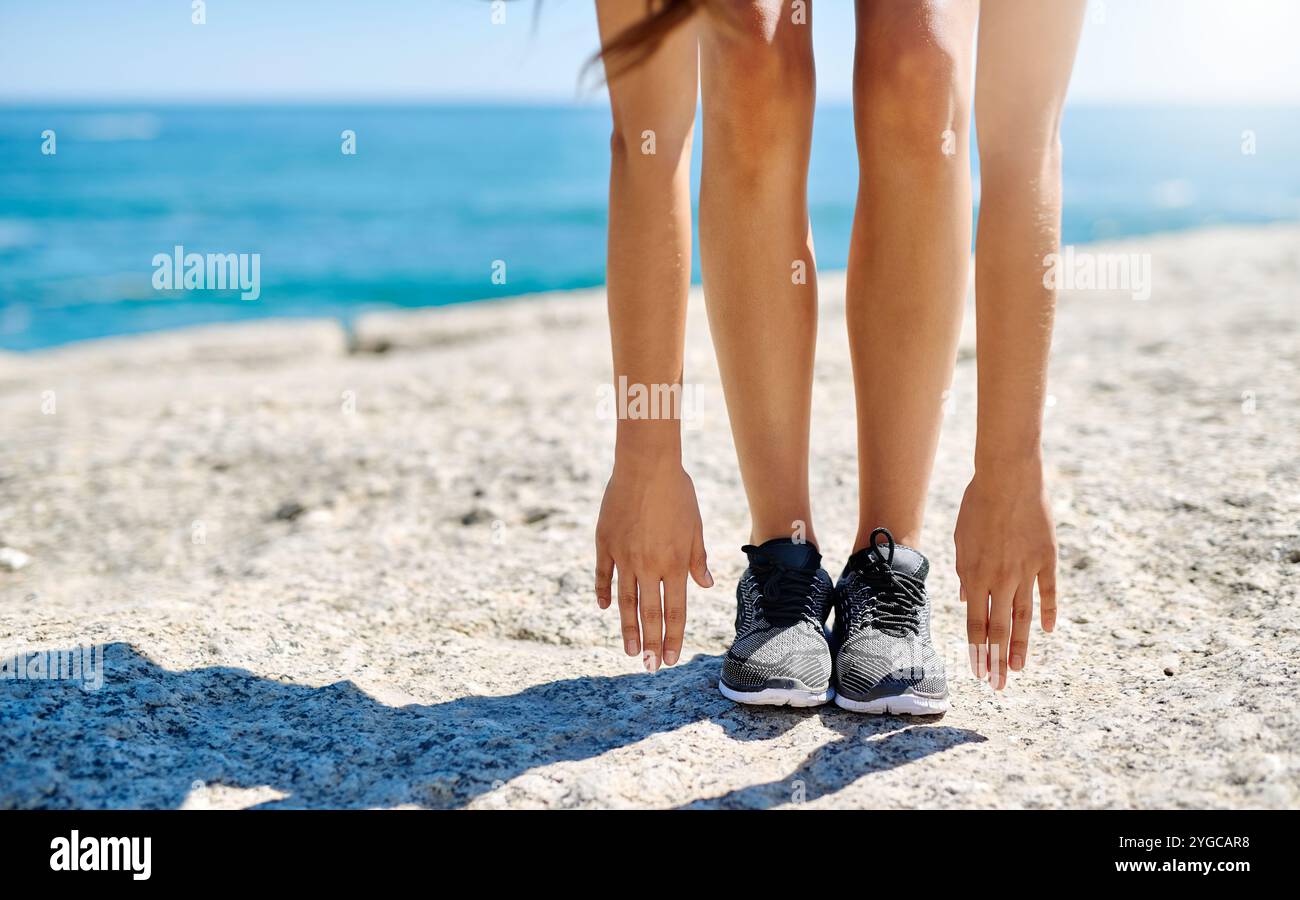 Woman, legs and stretching with hands on beach for fitness, exercise or ...