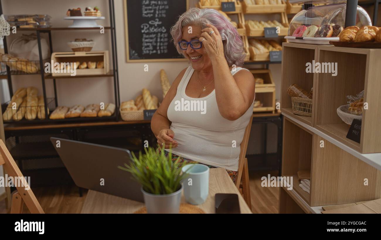 Mature grey haired woman smiling in a bakery shop surrounded by fresh ...