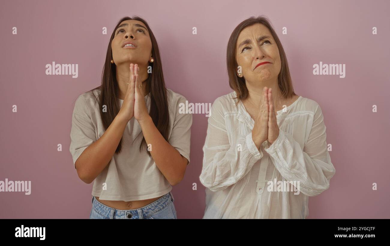 Mother and daughter praying together against a pink background ...