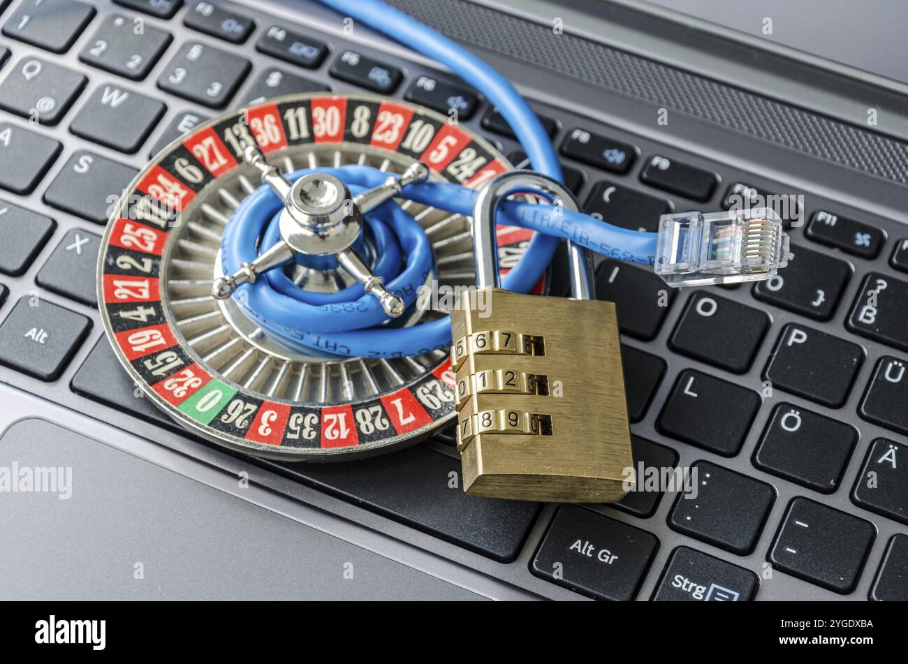 Roulette wheel, padlock and internet cable lying on computer keyboard symbolizing data encryption Stock Photo