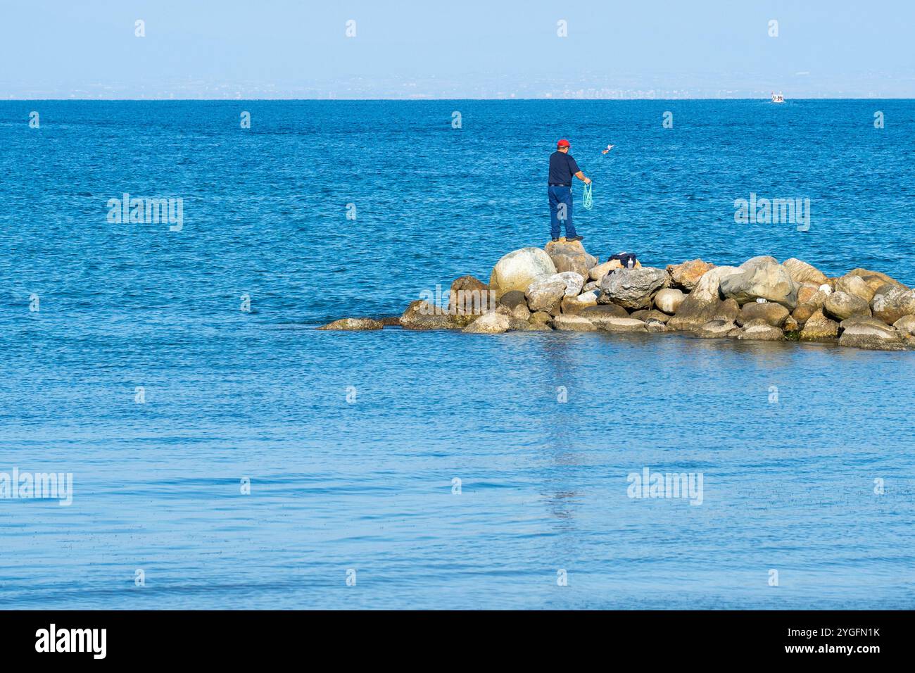 Fisherman Casting Net, Standing on Stone Pier by the Aegean Sea Under Clear Blue Sky. Stock Photo