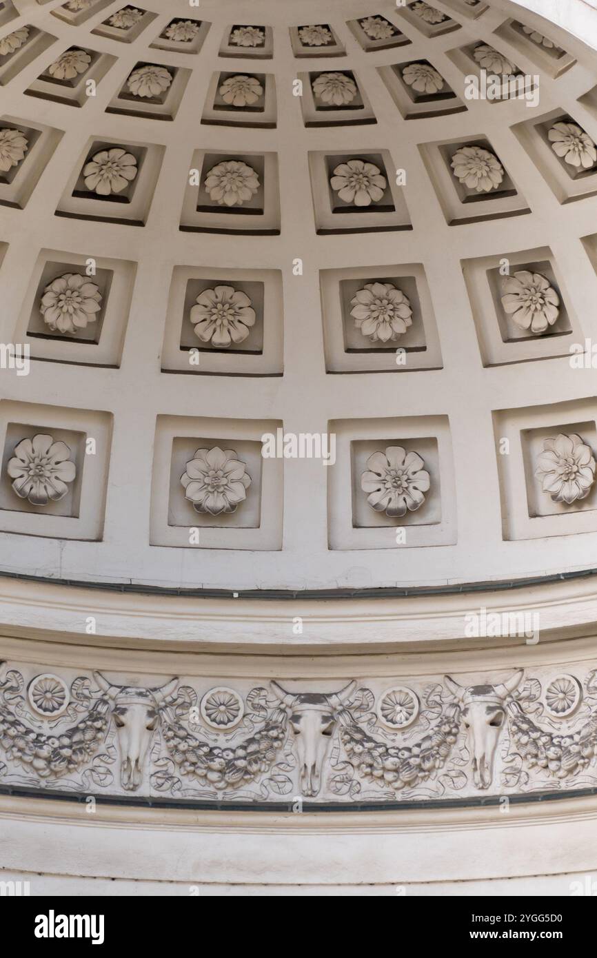 A domed ceiling decorated with flower reliefs in square frames and ornate garland motifs featuring cattle skulls. Details and elements of architecture Stock Photo