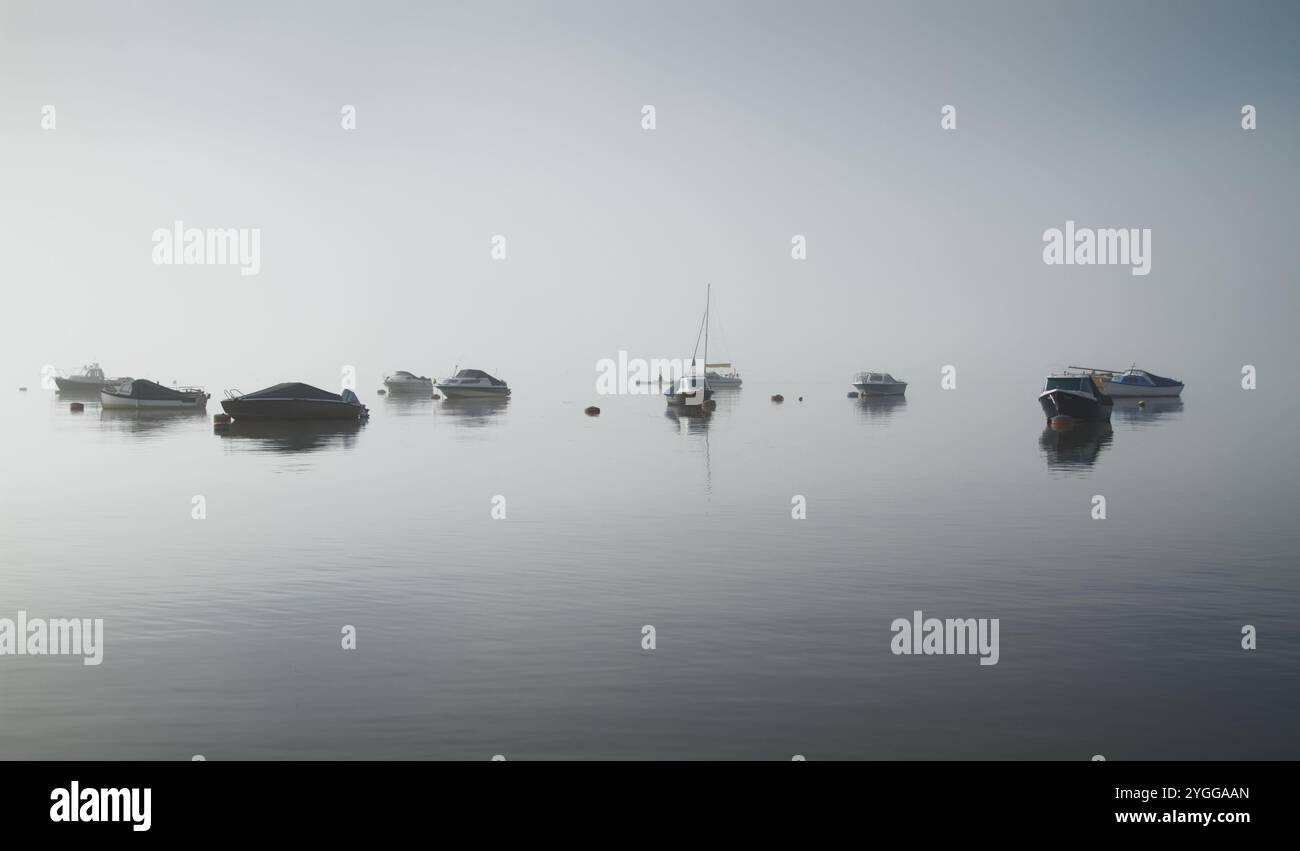 Motor Boats,Sailing Boats Anchored Moored In Christchurch Harbour On A Still, Calm Day With No Wind In Sea Mist, Fog, Christchurch, UK Stock Photo
