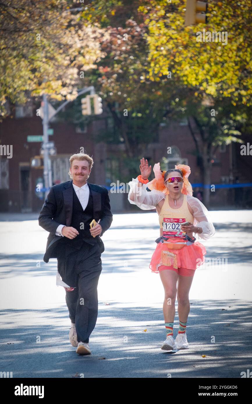 A couple running the 2024 New York Marathon in costumes and holding cell phones. On Bedford Ave in Williamsburg around the 10 mile mark. Stock Photo