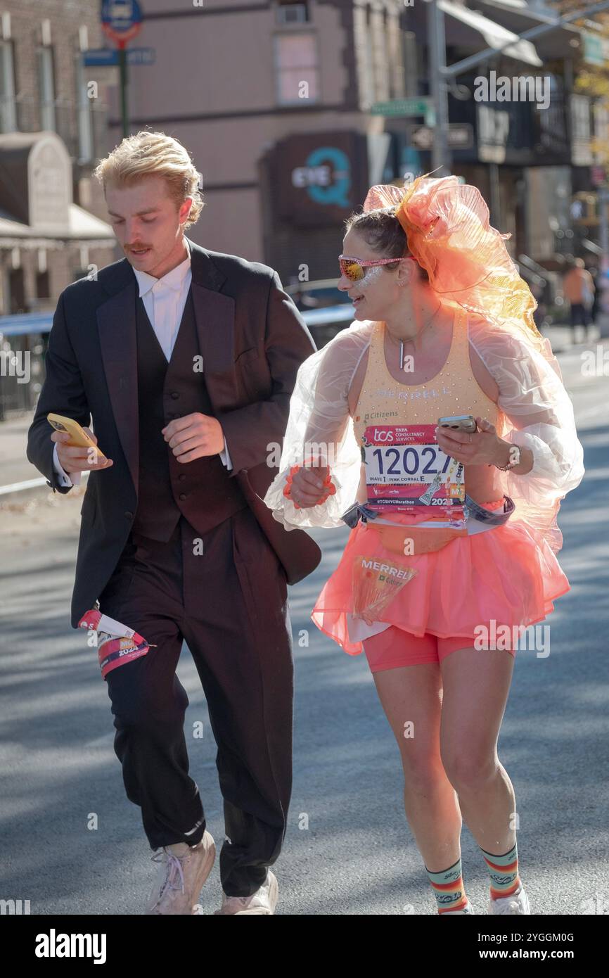 A couple running the 2024 New York Marathon in costumes and holding cell phones. On Bedford Ave in Williamsburg around the 10 mile mark. Stock Photo