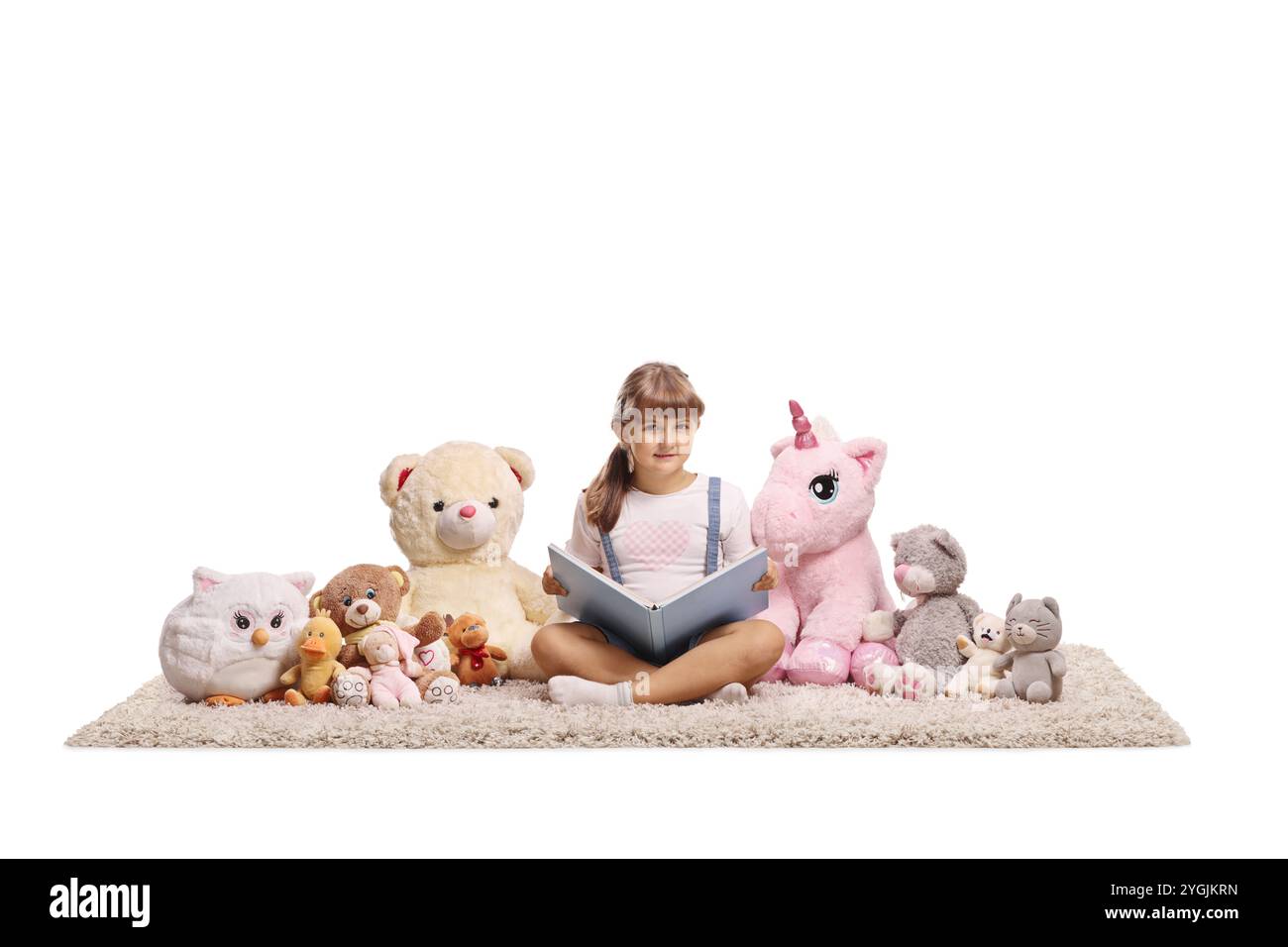 Little girl sitting on a carpet and reading a book to her plush animal ...