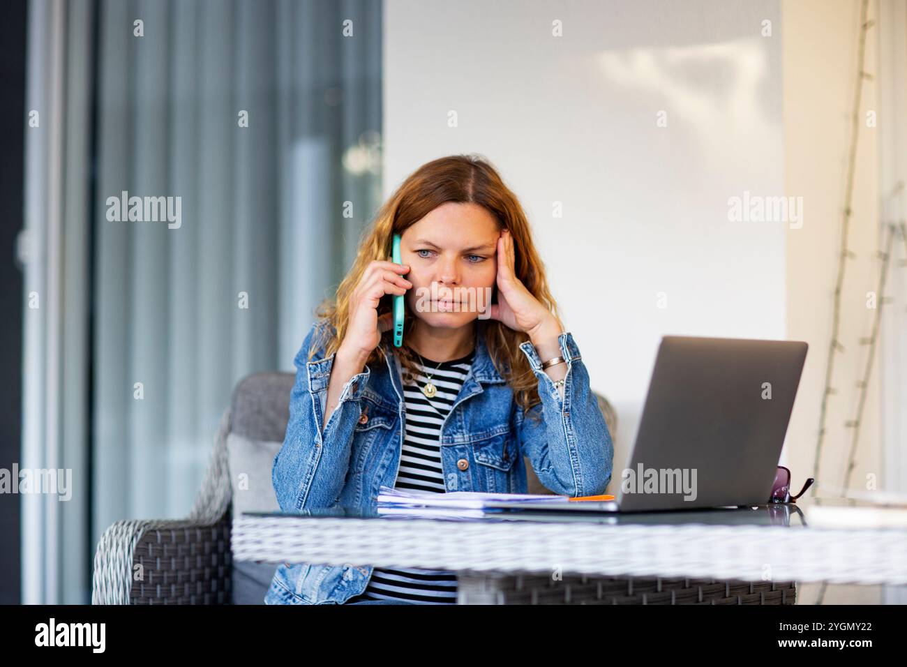 Woman talking on mobile phone while using laptop computer Stock Photo