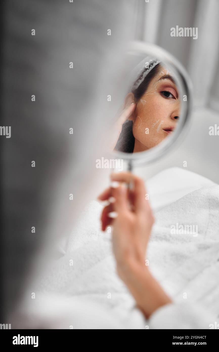 Young woman applying makeup while looking in a handheld mirror indoors Stock Photo