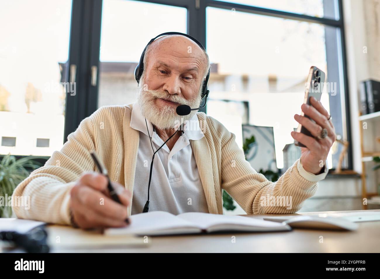 A senior businessman wearing smart casual clothes connects with colleagues, taking notes while working. Stock Photo