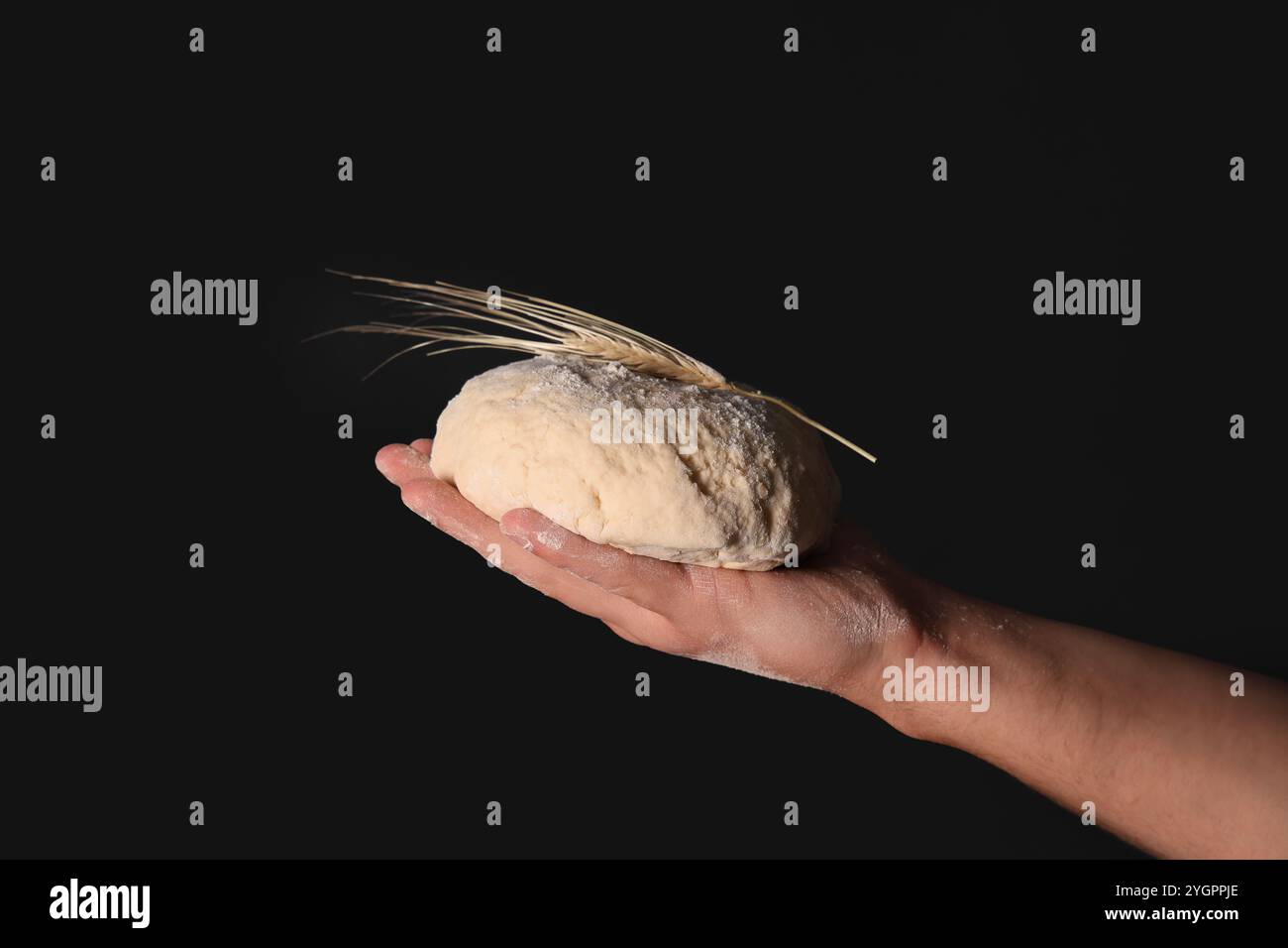 Male hand with fresh dough and wheat on black background Stock Photo