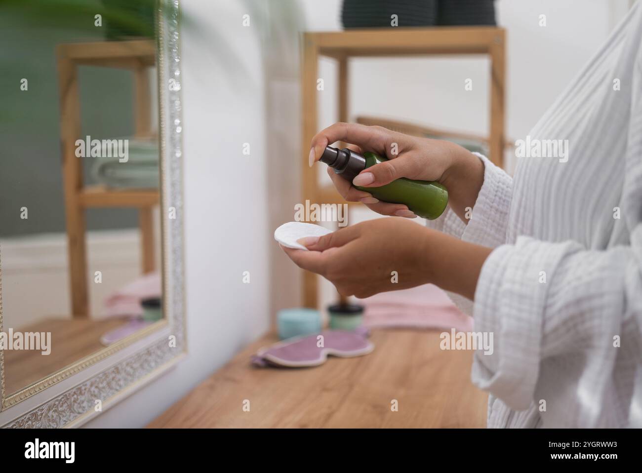 woman in bathroom, skincare regimen, dabs cleansing lotion onto a cotton pad beside the mirror. Stock Photo