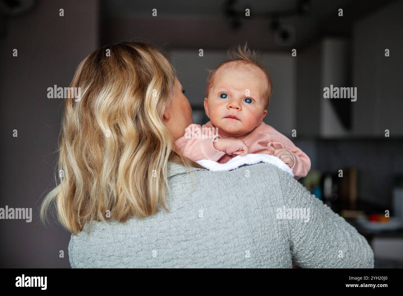 Caring mother holds small child upright while gently placing napkin on herself to keep clean, heartwarming moment of love and tenderness. Mom and newb Stock Photo