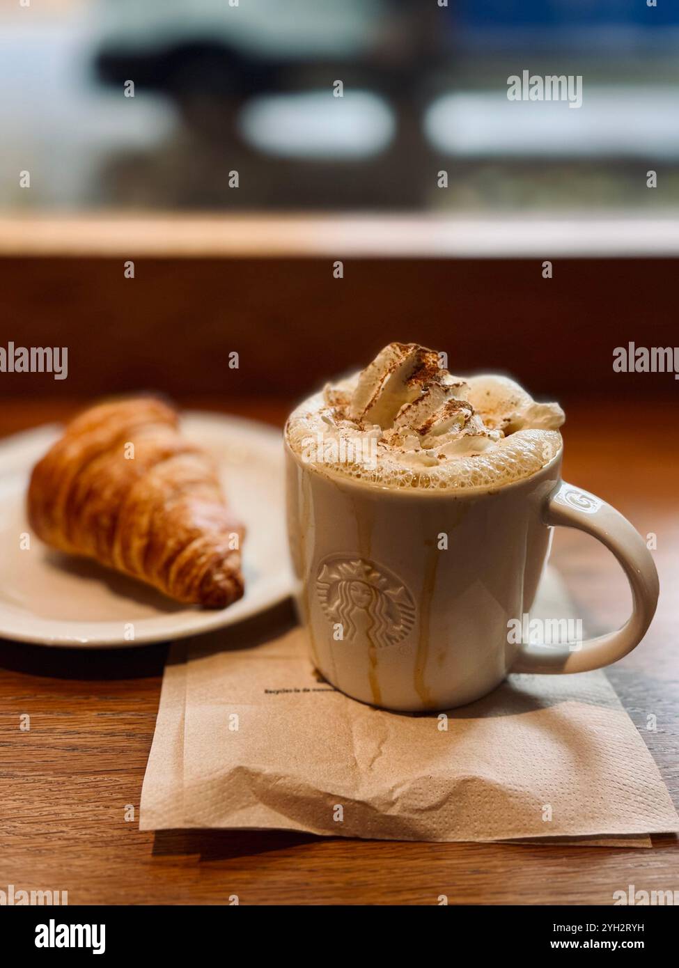 'A cozy morning scene featuring a frothy cappuccino topped with whipped cream and cinnamon alongside a flaky croissant, set on a wooden table.' - Smartphone Captured Stock Image