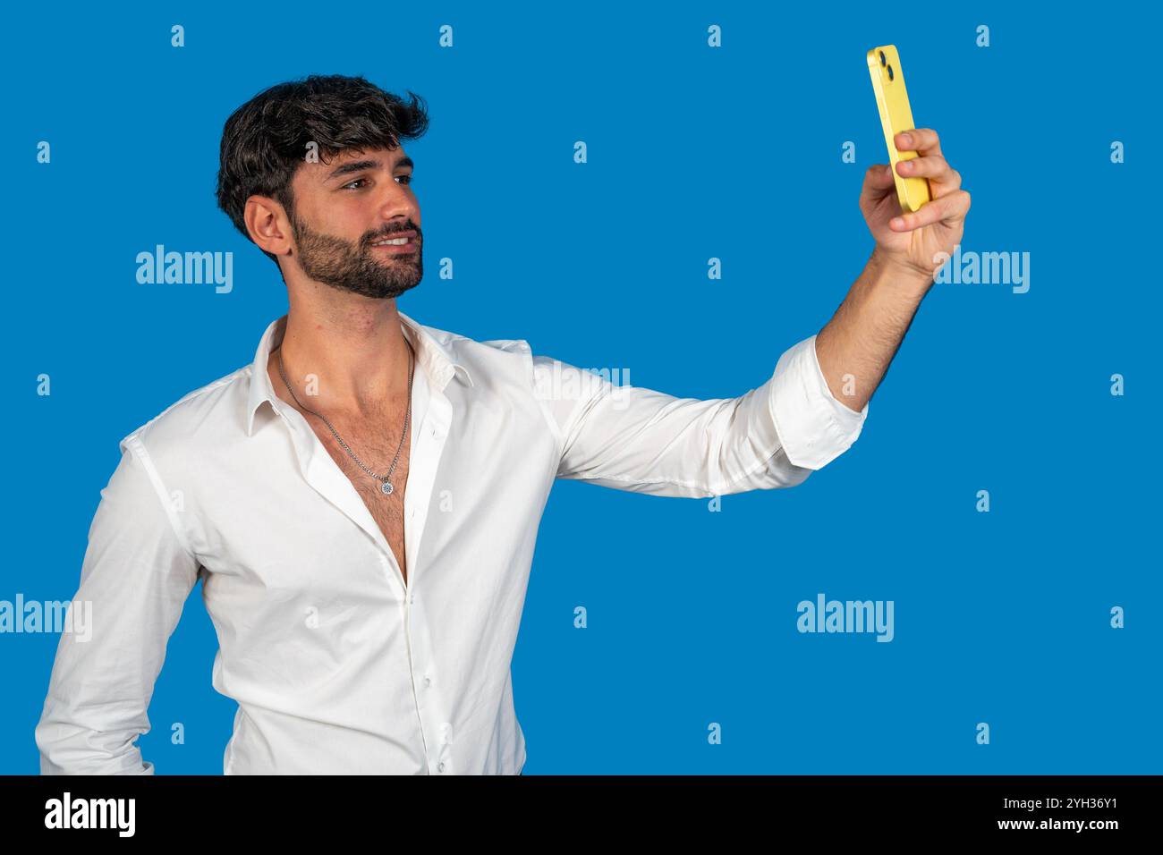 Young businessman taking a selfie with yellow smartphone on blue background Stock Photo