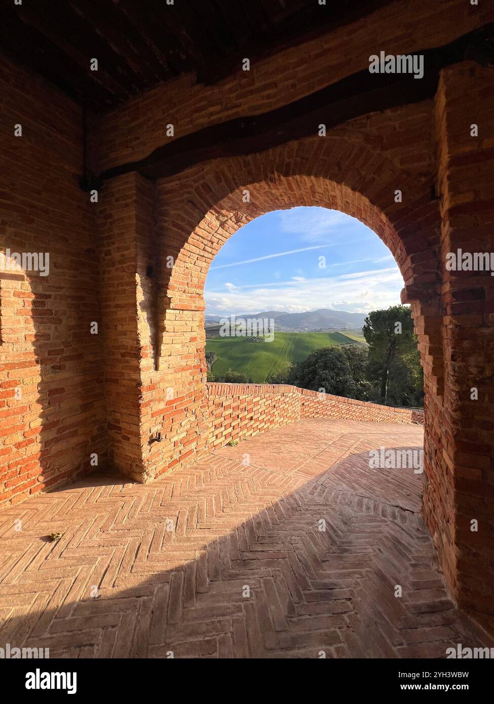 A rustic brick archway frames a scenic view of rolling green hills under a blue sky, capturing the charm of rural Italy. - Smartphone Captured Stock Image