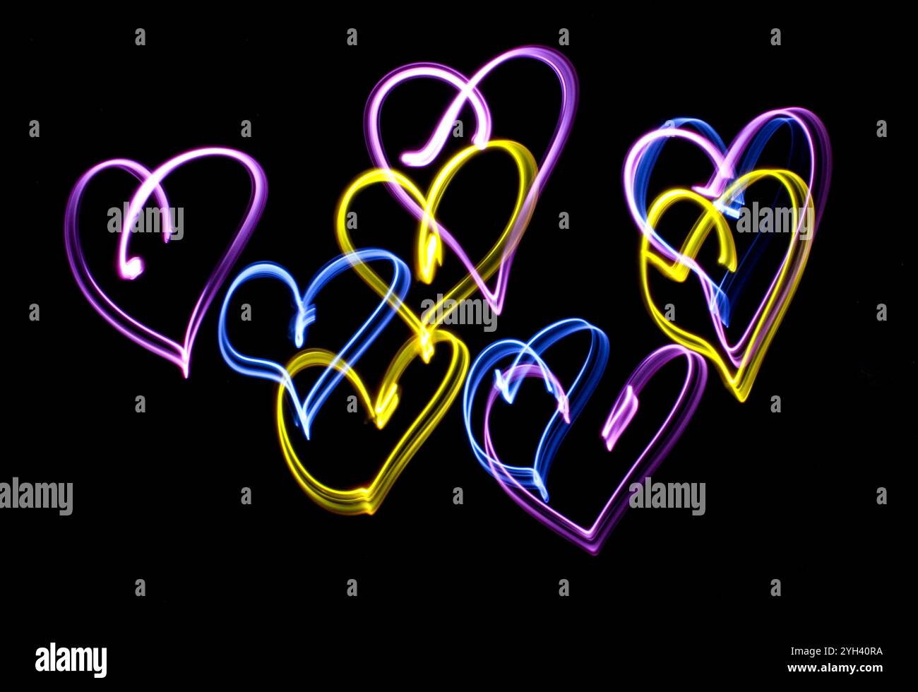 A long exposure photograph. Light painting photography, vibrant fairy lights drawing lots of colourful hearts against a black background Stock Photo