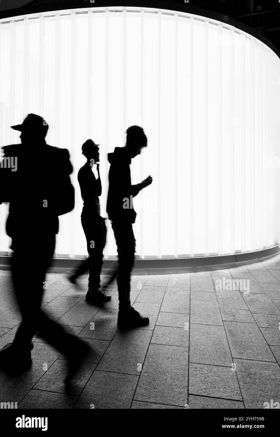 Silhouette of boys walking in front of illuminated white panel Stock Photo