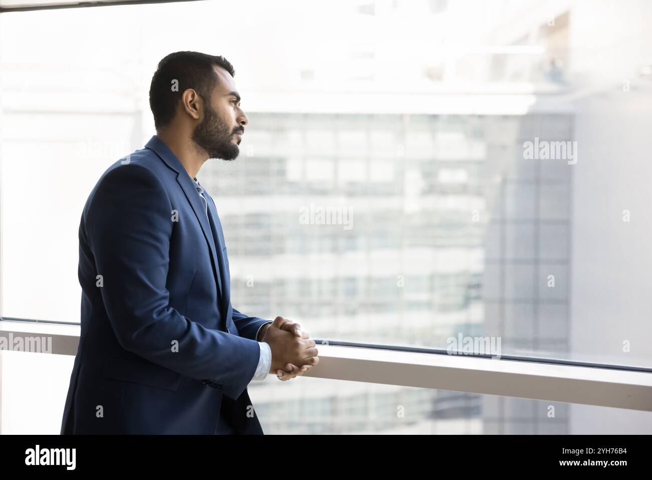 Pensive young Indian businessman standing at window Stock Photo