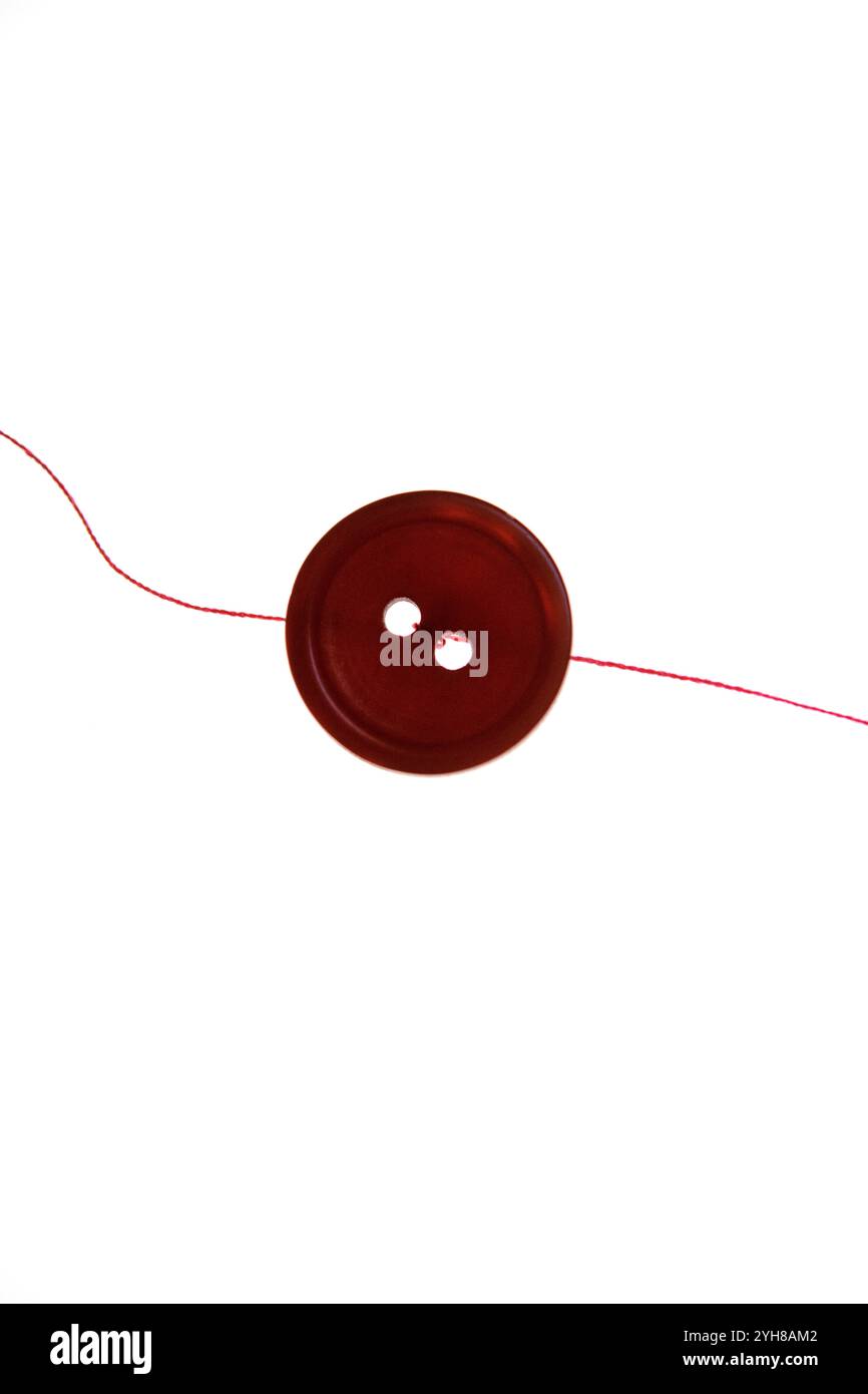 Still life of a single red button and a strand of red thread on a white background Stock Photo