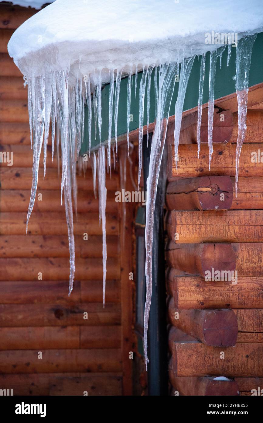 Dangling long icicles seen on the side of a stunning log cabin, home, house building with sharp edges in winter time season. Stock Photo