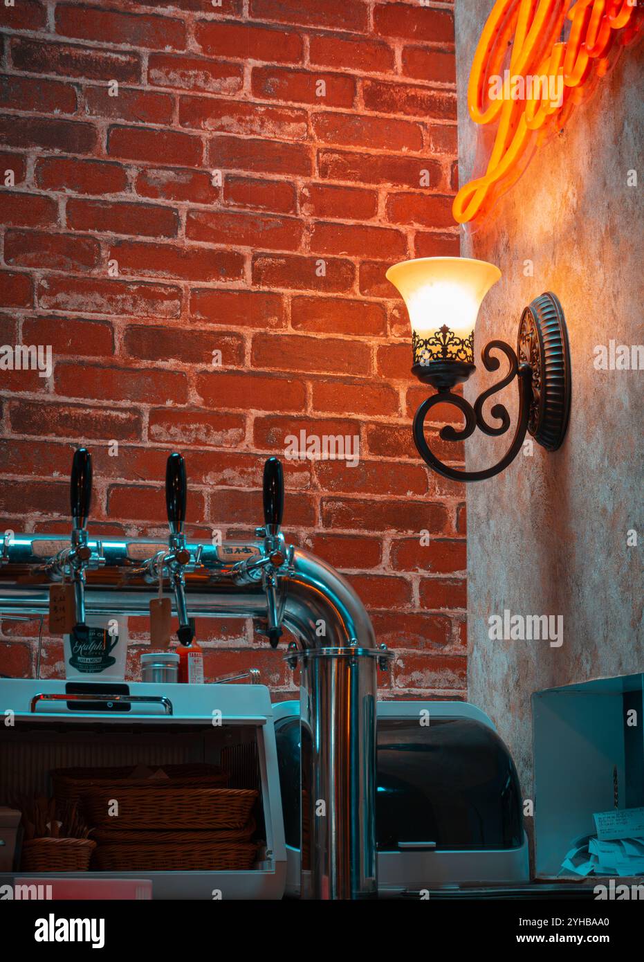 Vintage-style café interior with a glowing wall sconce, exposed brick wall, and beer taps, creating a cozy and inviting atmosphere Stock Photo