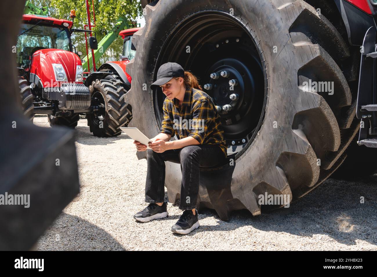 Female farm worker sitting on tractor wheel, using digital tablet at ...
