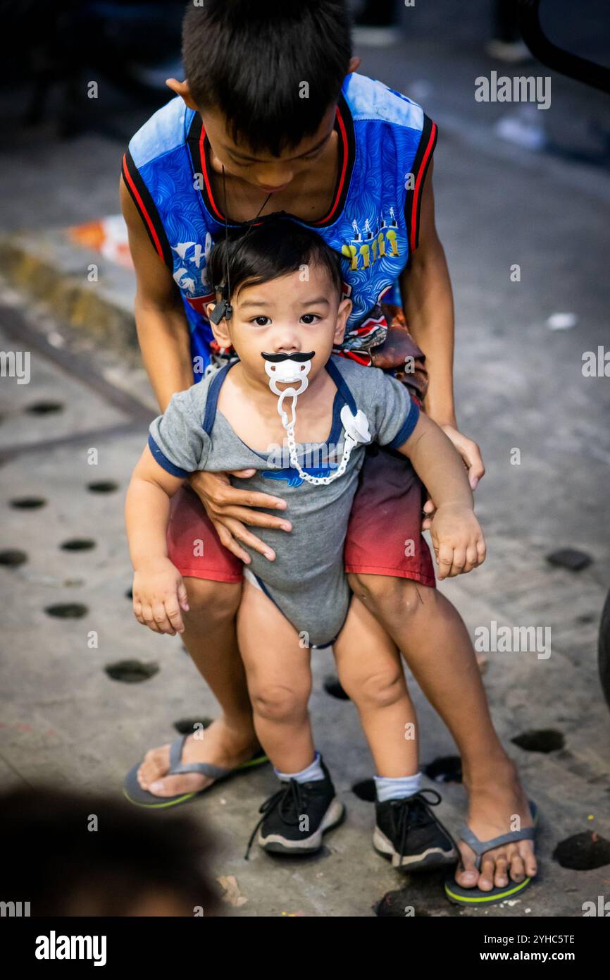 A young filipino boy plays with a baby, possibly his younger brother in the Ermita area of Manila, The Philippines. Stock Photo