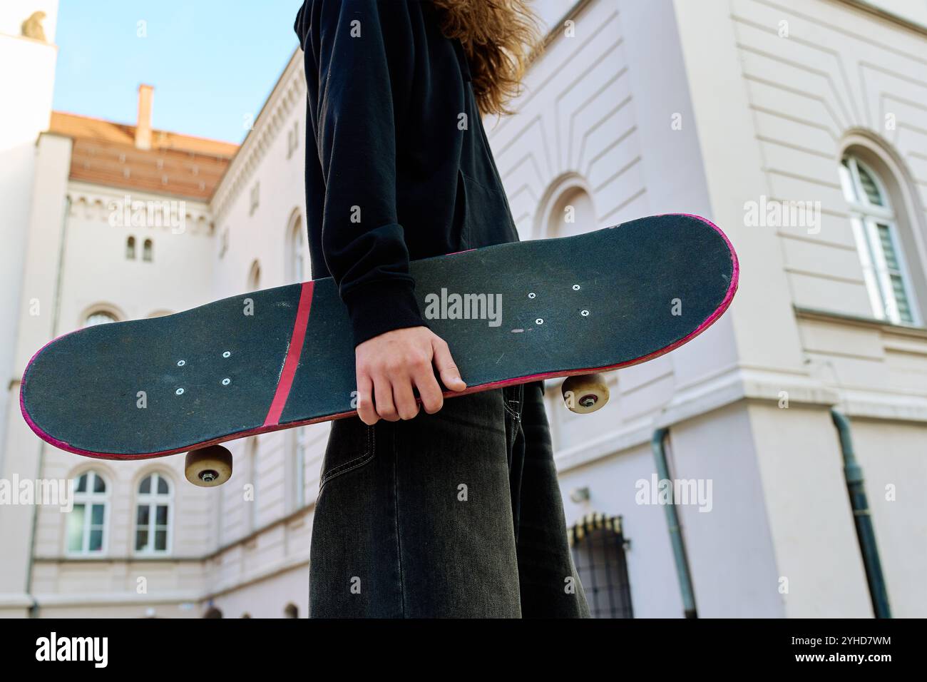 Skateboarder in baggy jeans holding scratched skateboard walking at ...