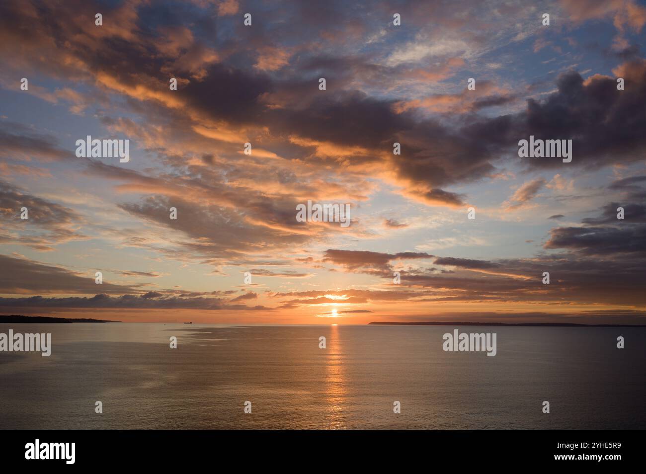 A beautiful sunset casts a warm glow over the tranquil ocean, with dramatic clouds . Stock Photo