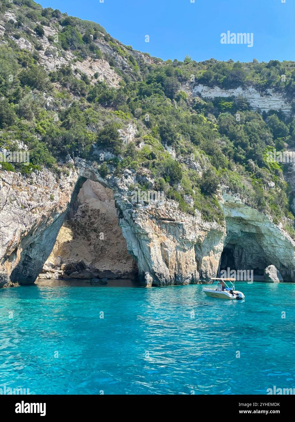 Peaceful seaside view from Parga, Greece, featuring clear waters, a boat, stones, and a beautiful hidden beach. - Smartphone Captured Stock Image