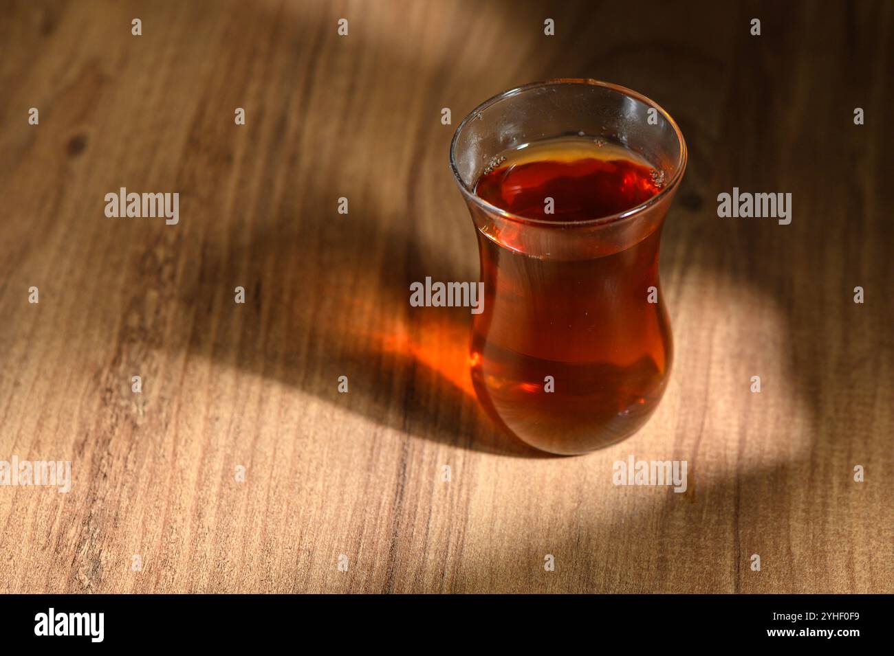 A glass filled with amber tea sits on natural wood, glowing softly in ...