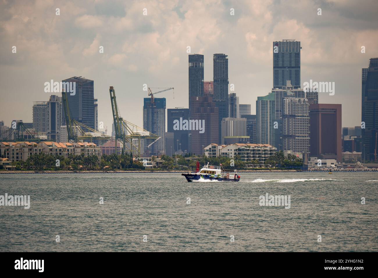 A singapore Marine port authority boat passes the docks and the edge of Sentosa as seen from the Singapore Strait with the city skyscrapers in the back. Stock Photo