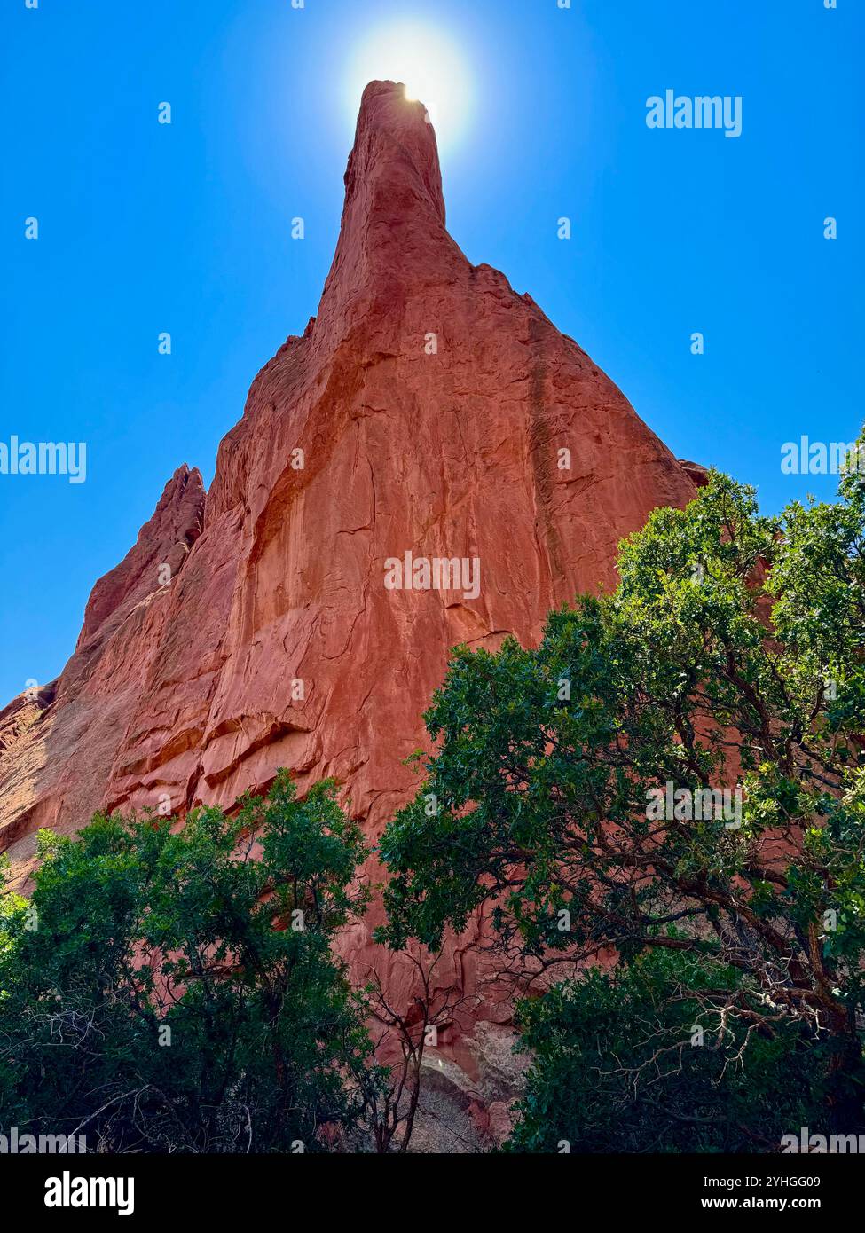A towering red rock formation reaches toward the sky, with the sun perfectly centered above, casting a glowing halo. - Smartphone Captured Stock Image