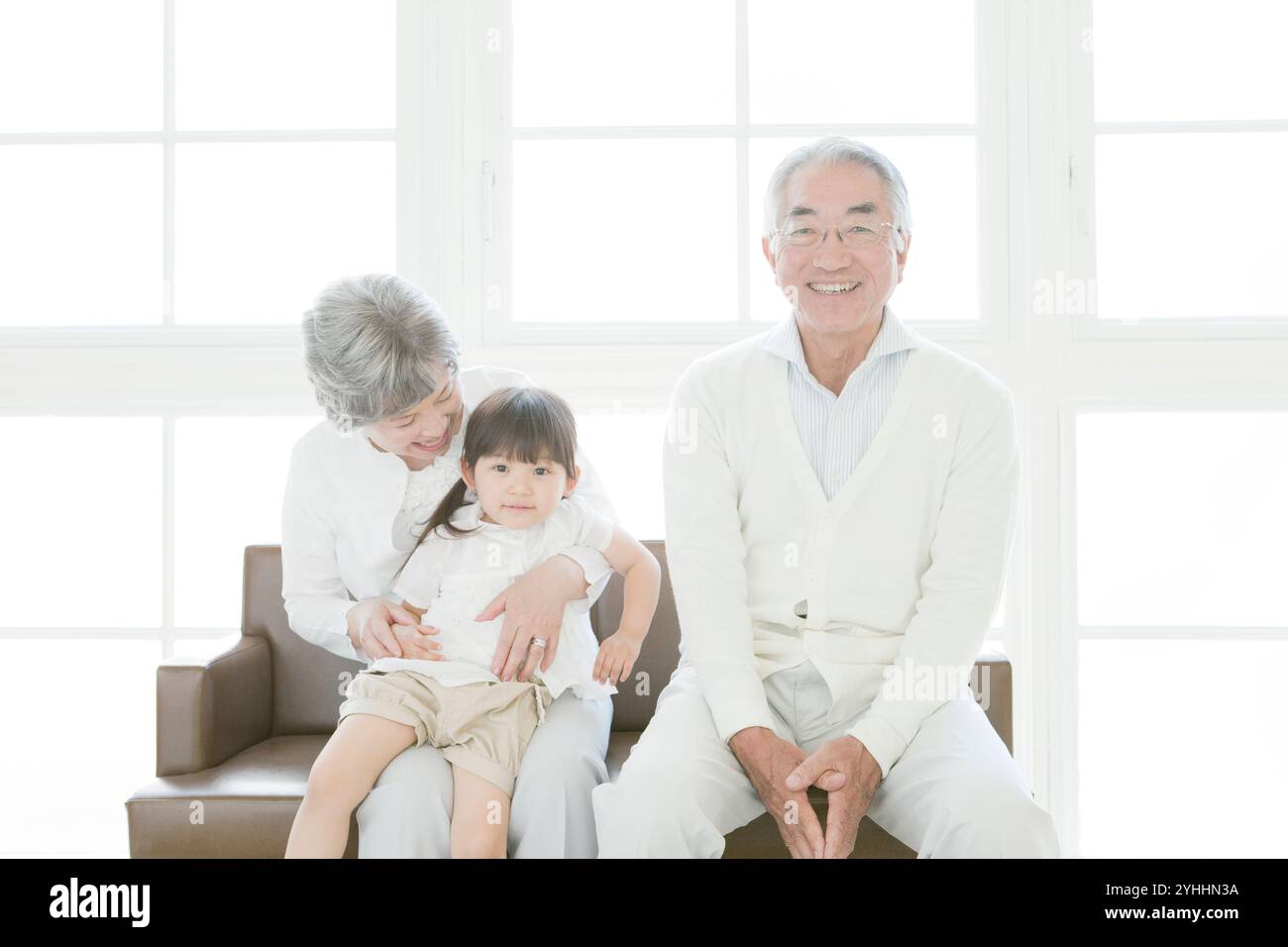 Granddaughter and senior couple sitting on sofa Stock Photo