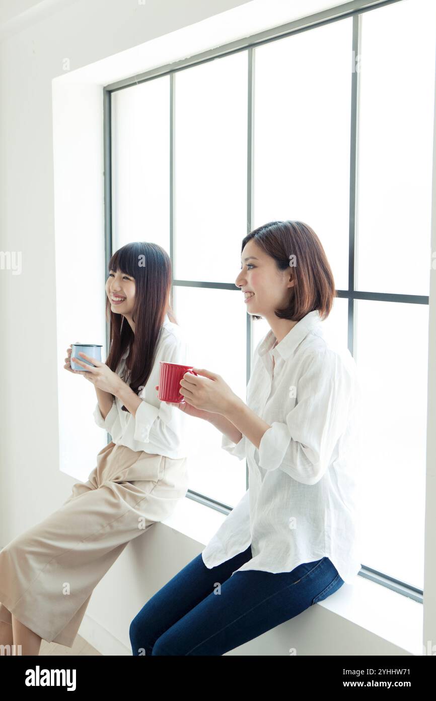 Two women in their 20s relaxing by the window Stock Photo - Alamy