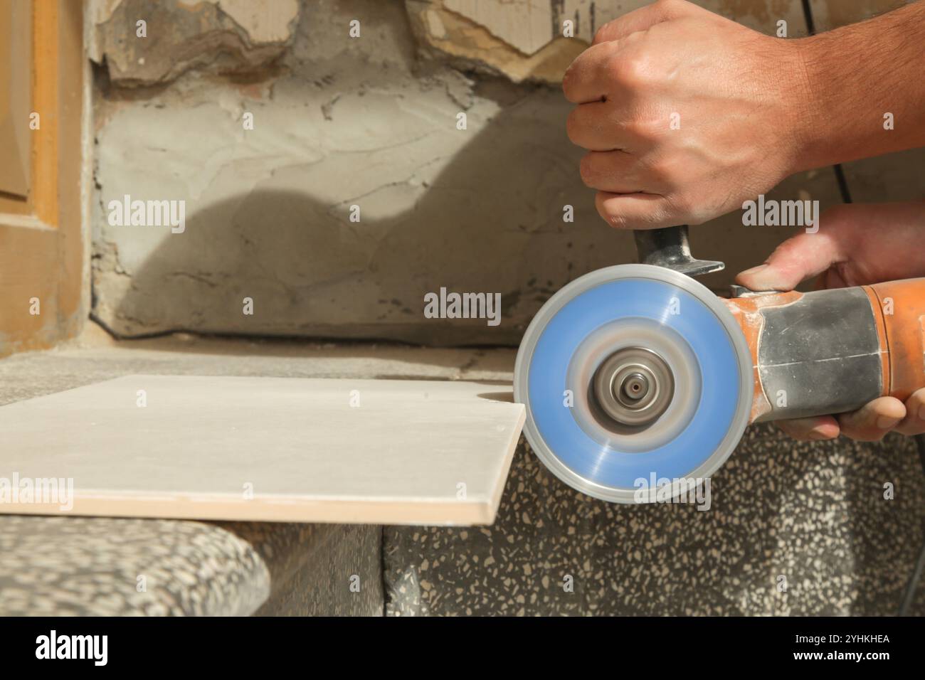 Worker cutting ceramic tile with disc grinder machine. DIY home improvement project. Stock Photo
