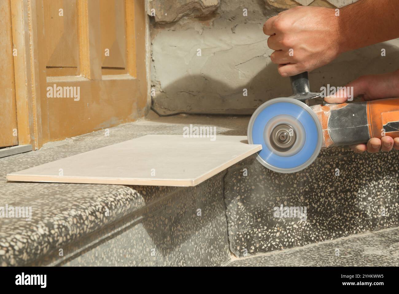 Worker cutting ceramic tile with disc grinder machine. DIY home improvement project. Stock Photo