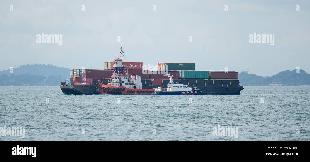 Capricorn 59 barge with containers aboard with Capricorn 80 tug boat alongside in the Singapore Strait being passed by a police boat. Singapore Asia Stock Photo